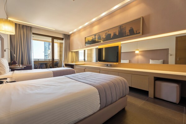 A hotel room with two beds, a TV, a desk, and a large window.
