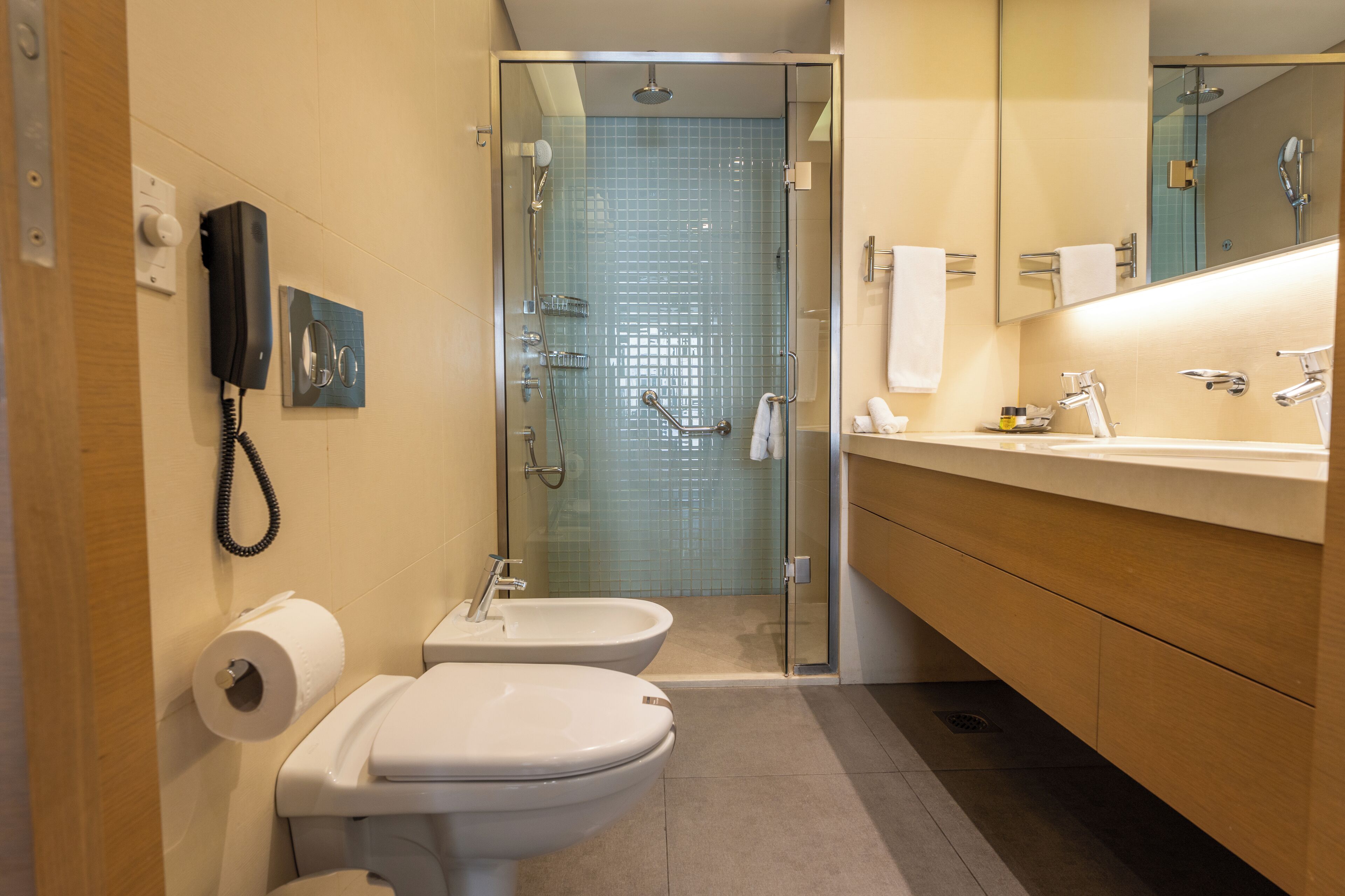 Un baño moderno con ducha de vidrio, inodoro, bidés, lavabo y espejo.