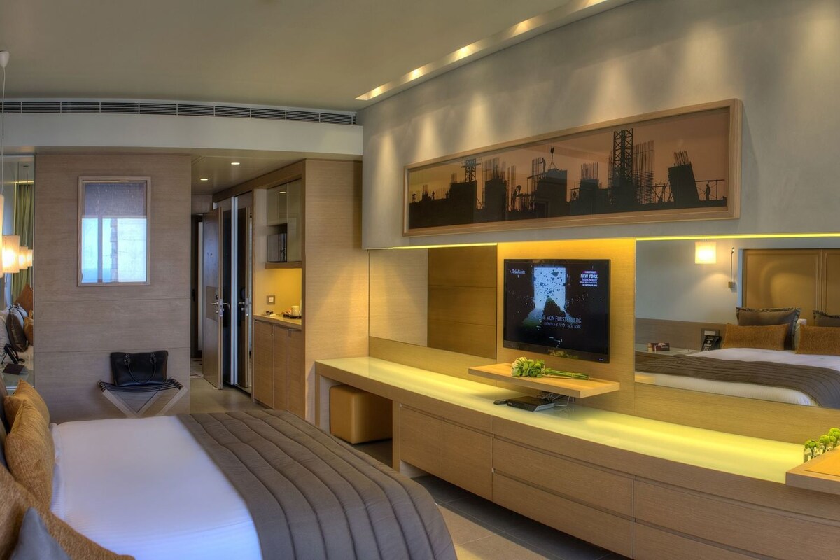 Ein modernes Hotelzimmer mit einem großen Bett, einem Fernseher, einem Schreibtisch und einer Sitzecke.