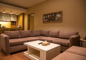Una sala de estar con un sofá seccional marrón, una mesa de centro blanca y un reloj fijado a la pared.
