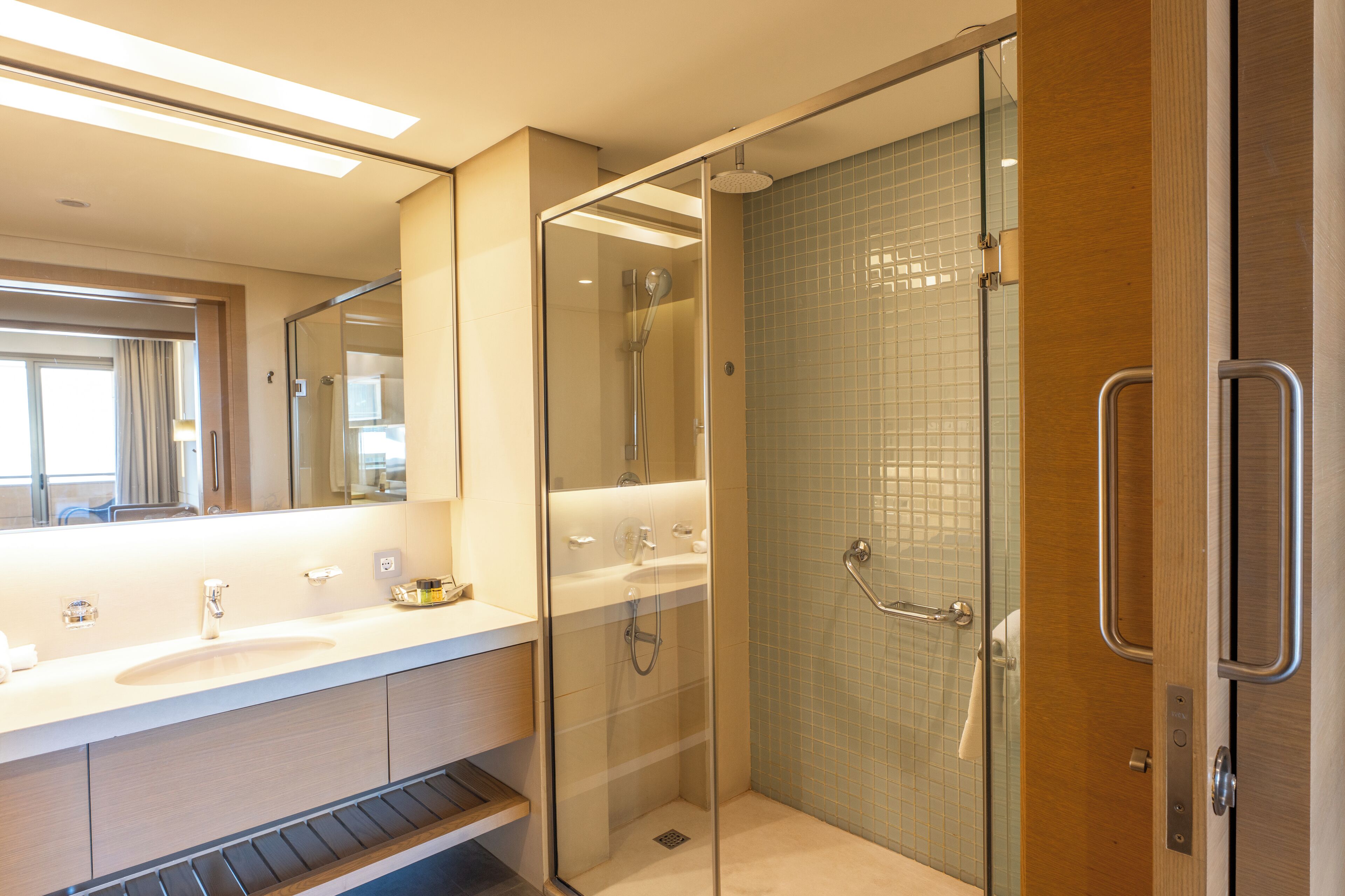 Un baño moderno con ducha envuelta en vidrio, un espejo grande y una encimera con lavamanos y tocador.