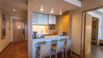 Una cocina moderna con una isla central, armarios empotrados y un microondas. Hay tres sillas alrededor de la isla y una puerta que da a un armario.