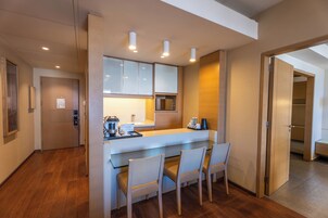 Una cocina moderna con una isla central, armarios empotrados y un microondas. Hay tres sillas alrededor de la isla y una puerta que da a un armario.