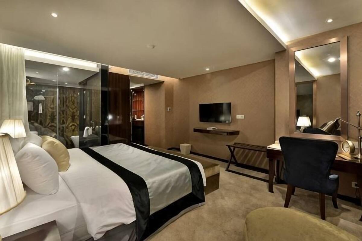 A hotel room with a bed, desk, chair, TV, and a mirror.