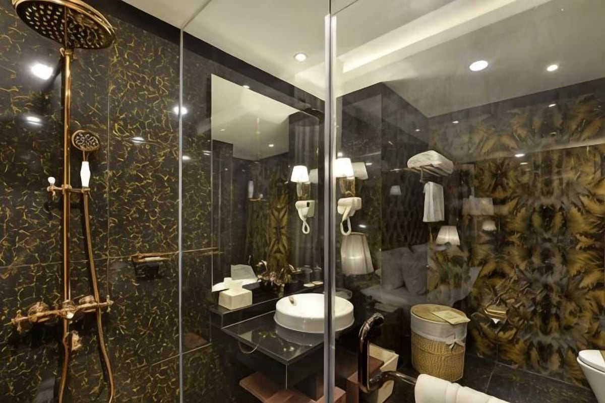 Un baño moderno con un espejo grande, un cabezal de ducha dorado, un lavabo redondo y una pared de mármol.
