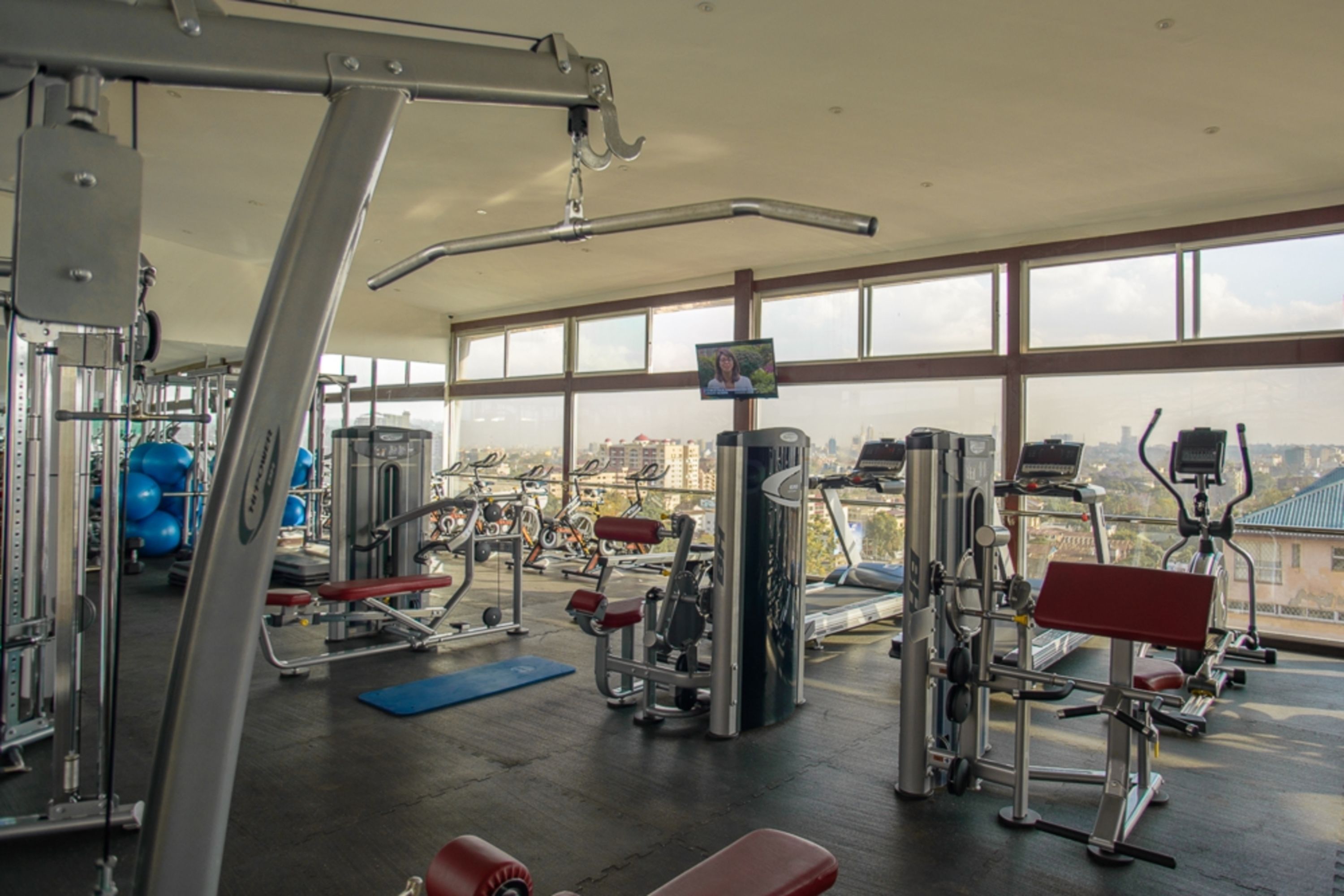Une salle de sport équipée de divers appareils d’exercice, dotée de grandes fenêtres et offrant une vue sur la ville.