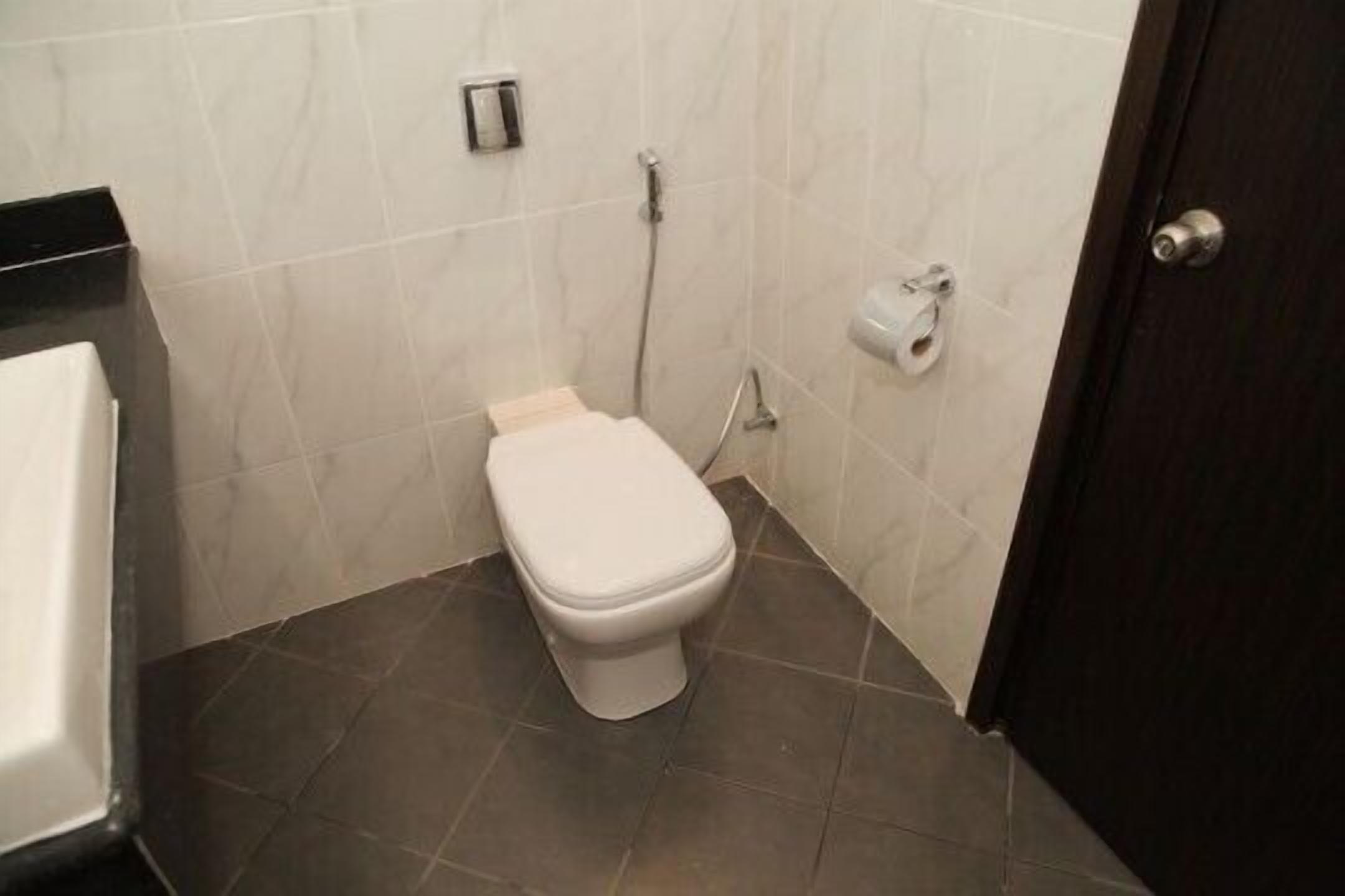A small bathroom with a white toilet, a towel dispenser, and a toilet paper holder on the wall.