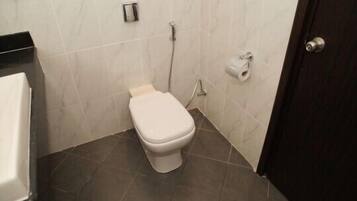 A small bathroom with a white toilet, a towel dispenser, and a toilet paper holder on the wall.