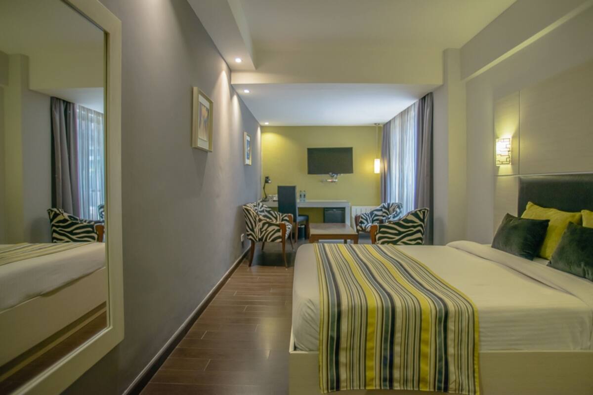 A hotel room with a large bed, a desk, two chairs, a mirror, and a television.