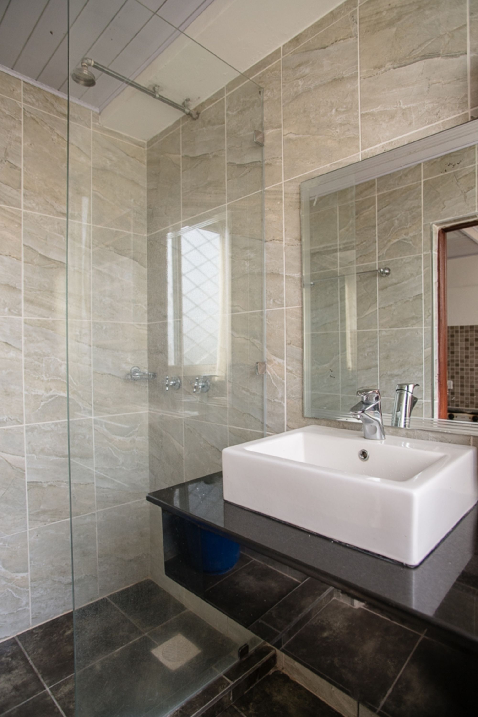 A modern bathroom with a glass-enclosed shower, a white sink, and a large mirror.