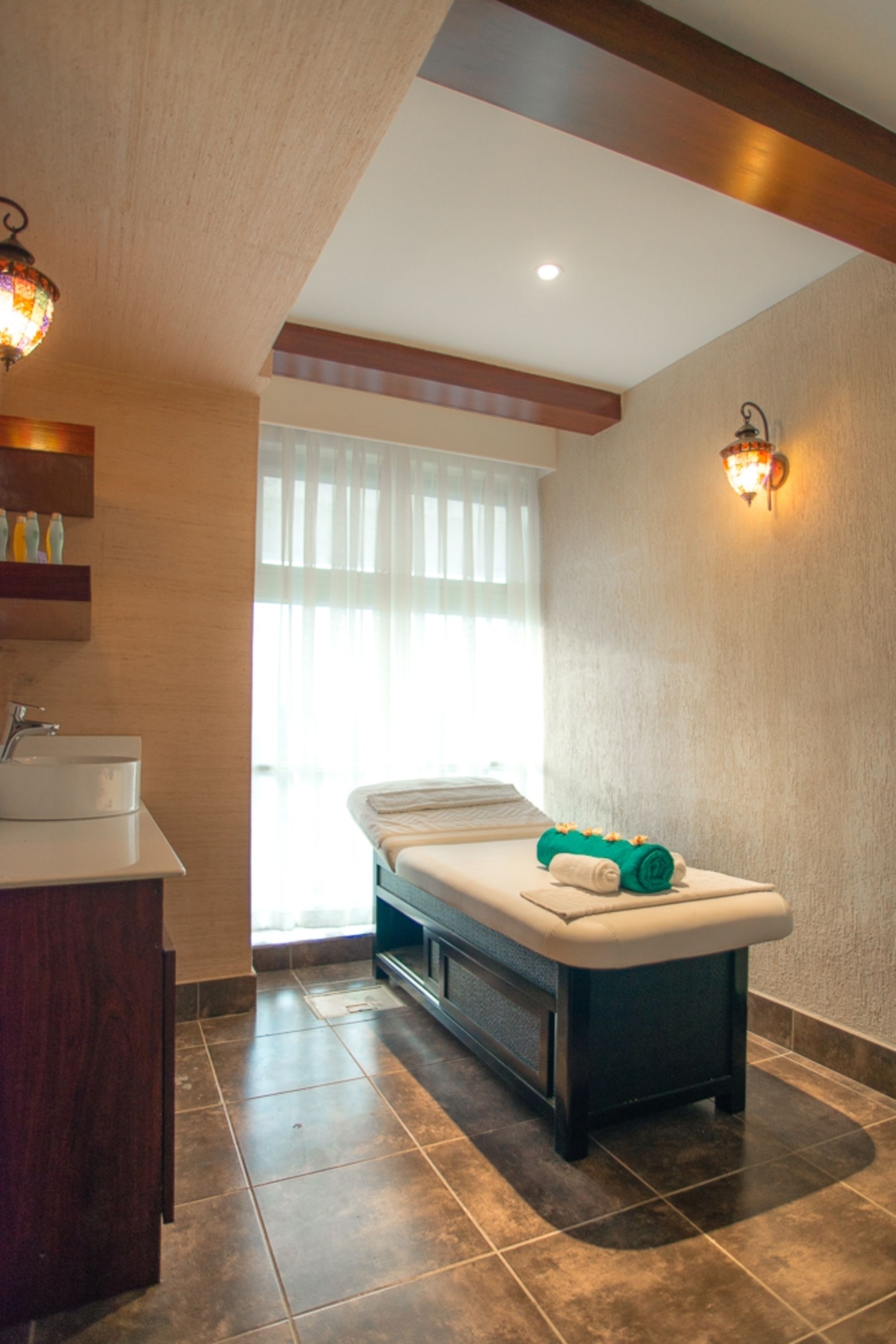 A spa room with a massage table, a sink, and a window with curtains.