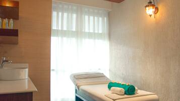 A spa room with a massage table, a sink, and a window with curtains.