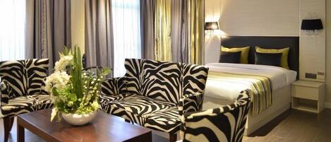 A hotel room with a zebra-patterned sofa set, a bed with a gold and black headboard, and a bedside table with a lamp.