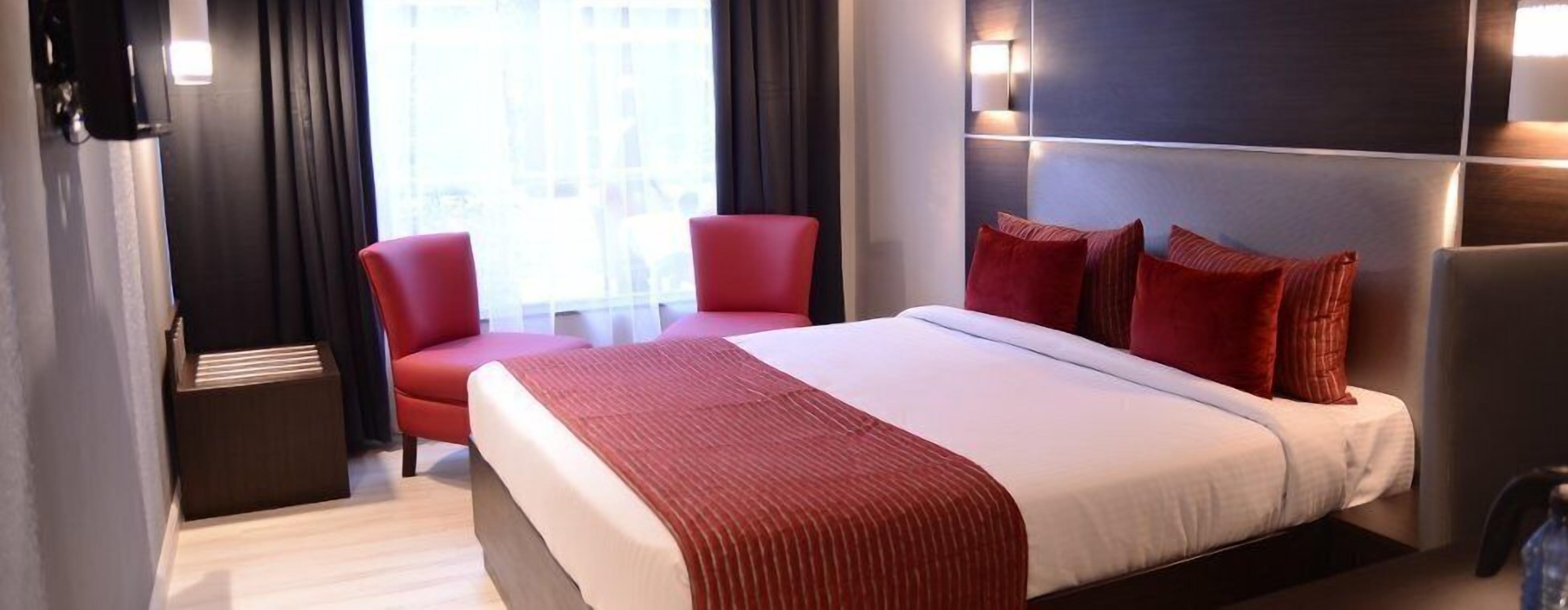 A hotel room with a large bed, red chairs, and a modern design.