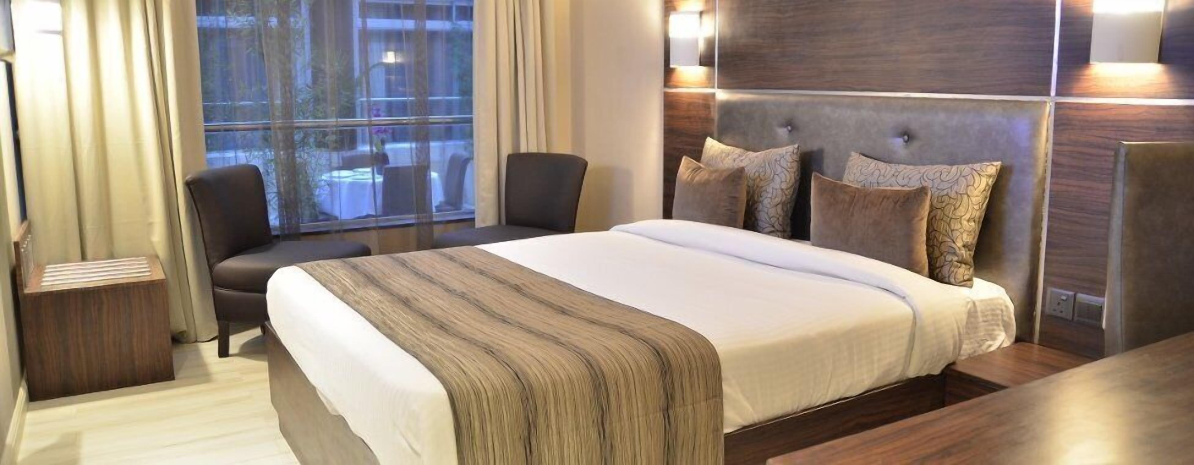 A hotel room with a large bed, two chairs, a bedside table, and a view of the outdoors through a window.