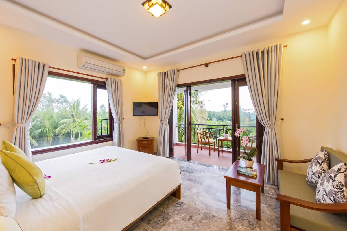A hotel room with a large bed, a balcony with a table and chairs, and a TV on the wall.