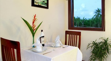 Una mesa de comedor dispuesta con una botella, vasos y una servilleta, con vistas a follaje por la ventana.