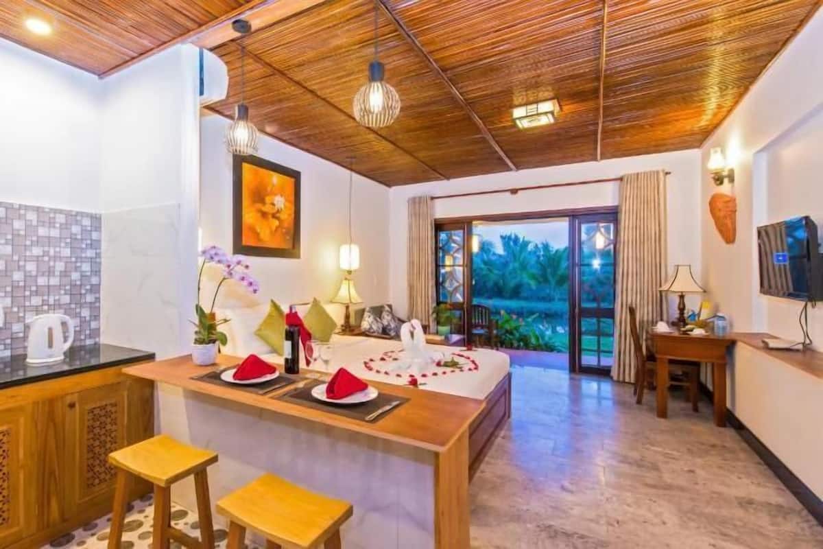 A modern kitchen with a wooden ceiling, a dining area with a table set for two, and a view of the outdoors.