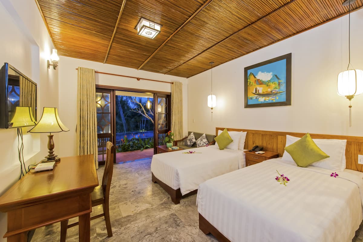 A hotel room with two beds, a desk, a chair, a wooden ceiling, and a painting on the wall.