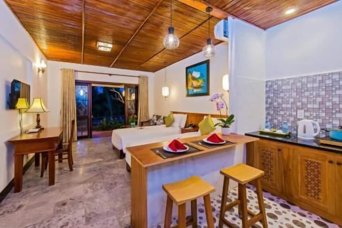 A hotel room with a wooden ceiling, a bed, a small kitchen area, and a sliding glass door leading to a balcony.