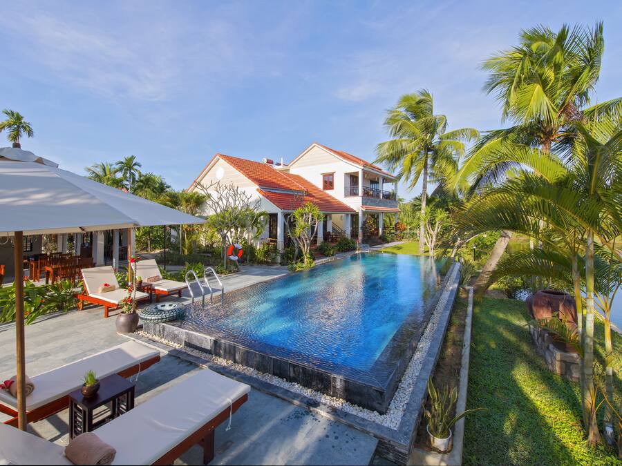 Une piscine avec des chaises longues, une maison et des palmiers.