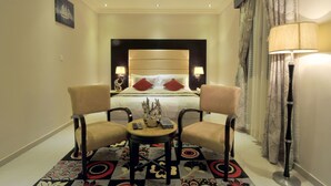 Une chambre d’hôtel avec un grand lit, deux fauteuils, une petite table et une lampe sur pied.