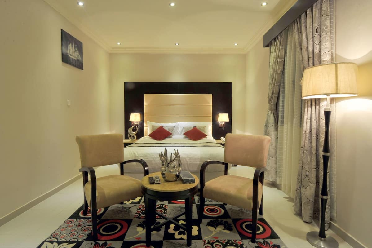 A hotel room with a large bed, two armchairs, a small table, and a floor lamp.
