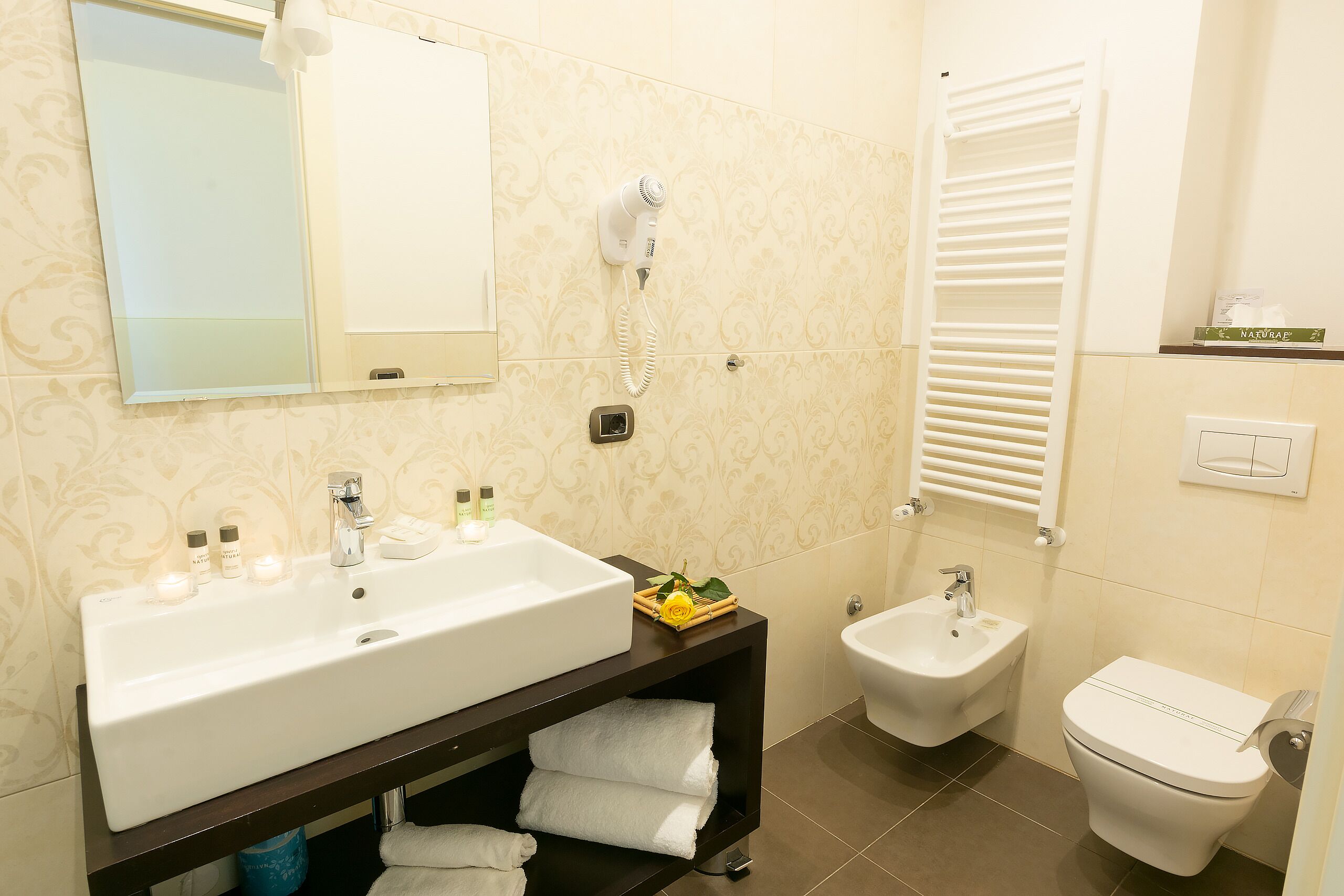 Un baño con un lavamanos grande de color blanco, un bidé, un inodoro y un secador de pelo montado en la pared.