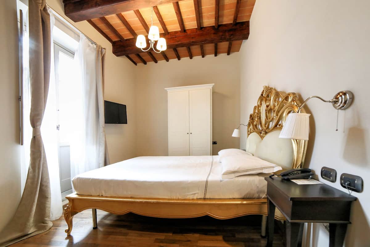 A bedroom with a wooden bed frame, a bedside table with a lamp, a wardrobe, and a chandelier.