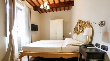 A bedroom with a wooden bed frame, a bedside table with a lamp, a wardrobe, and a chandelier.
