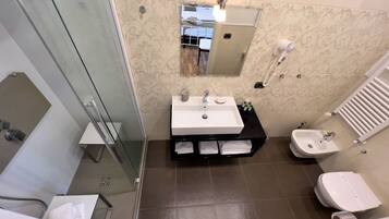 A modern bathroom with a glass shower enclosure, a white sink with a vanity, a bidet, and a toilet.