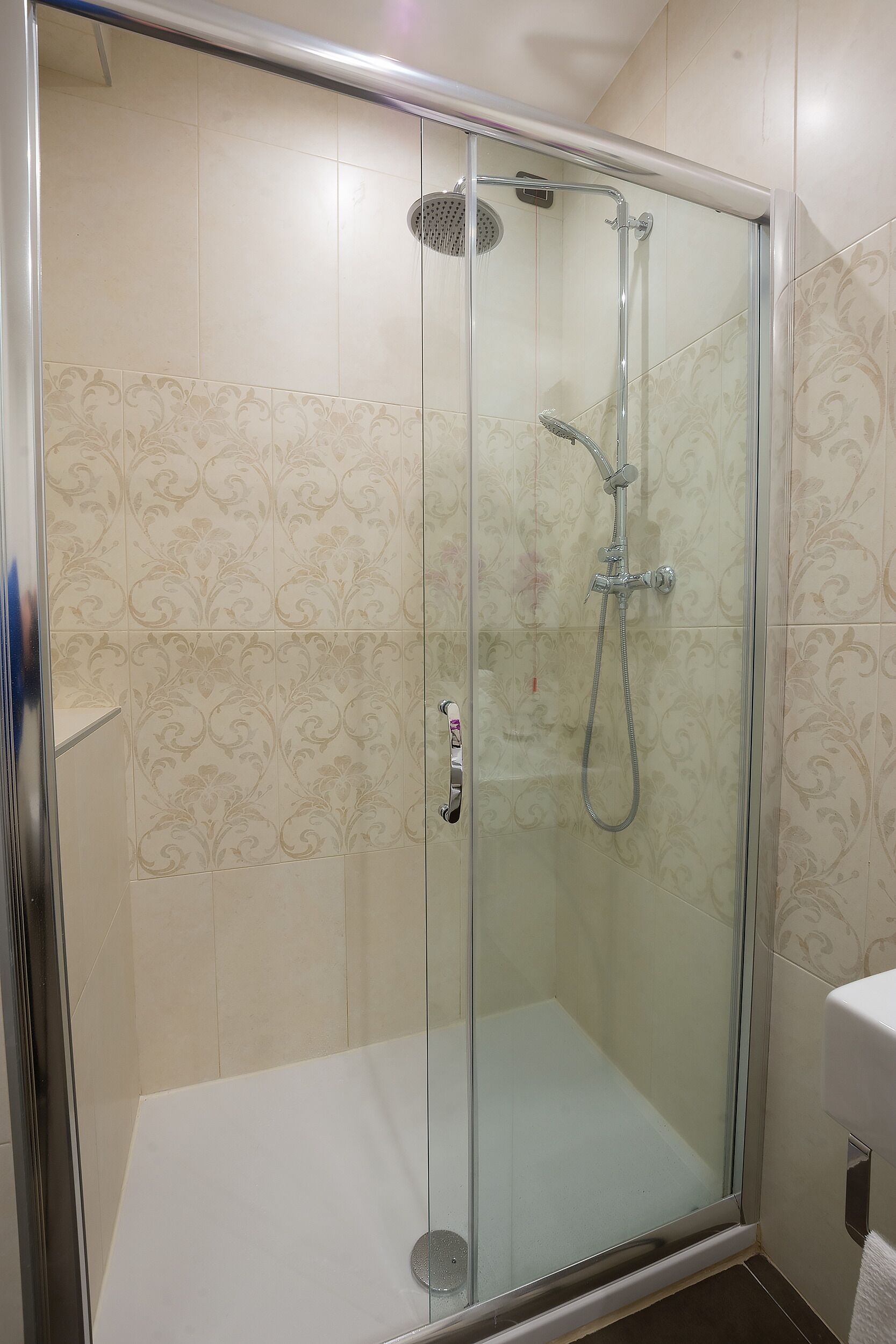 Ducha con cerramiento de vidrio, cabezal de ducha de mano y grifo empotrado.