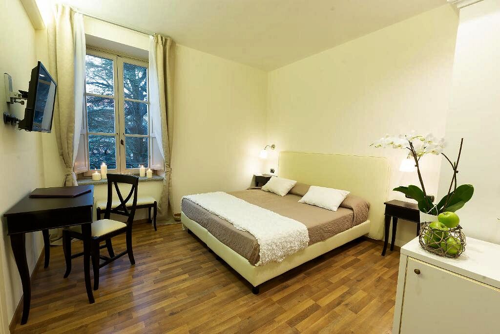 Une chambre à coucher avec un lit, un bureau, une chaise, une petite table, une fenêtre et une plante.