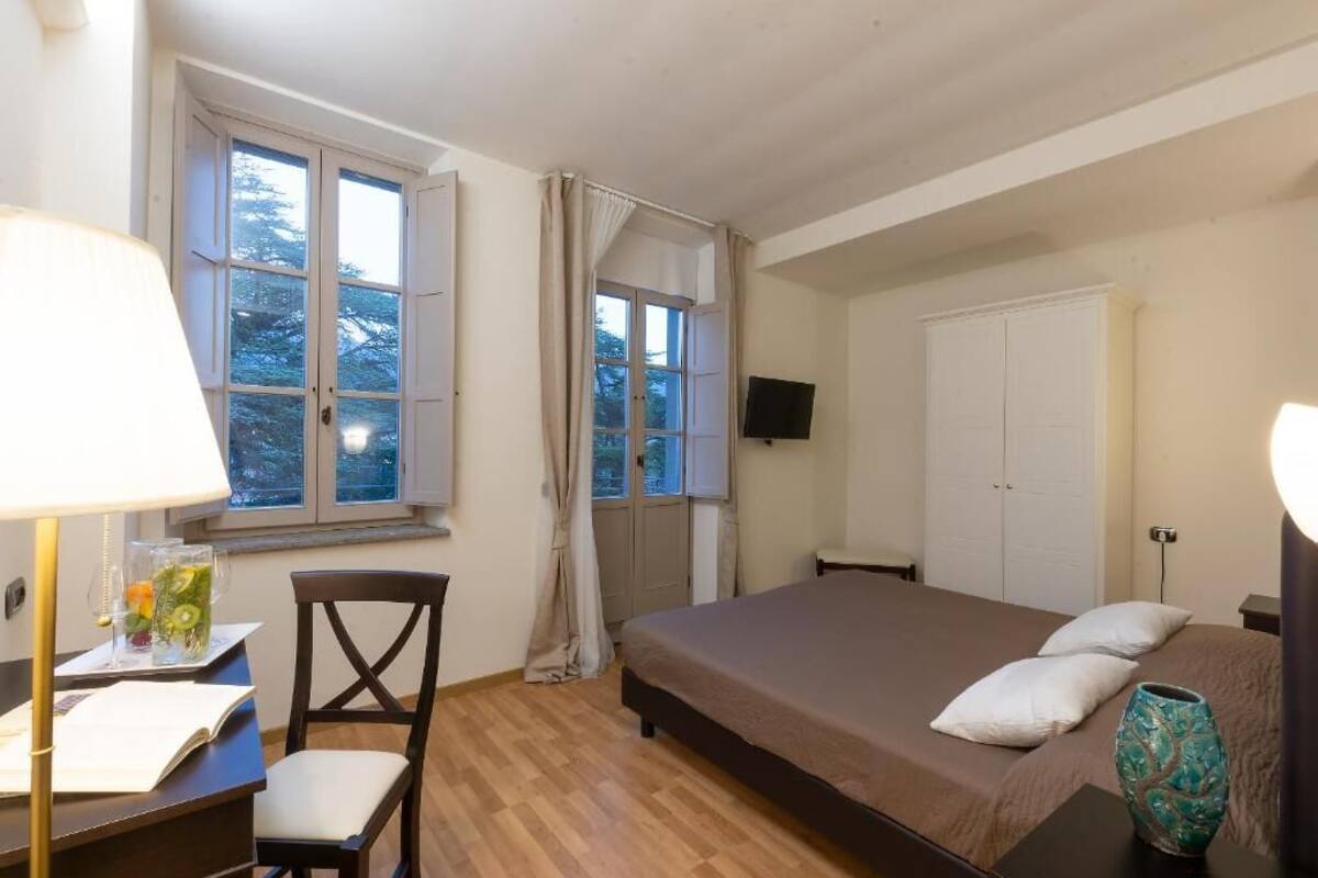 A bedroom with a bed, a desk with a lamp, a chair, and a window with curtains.