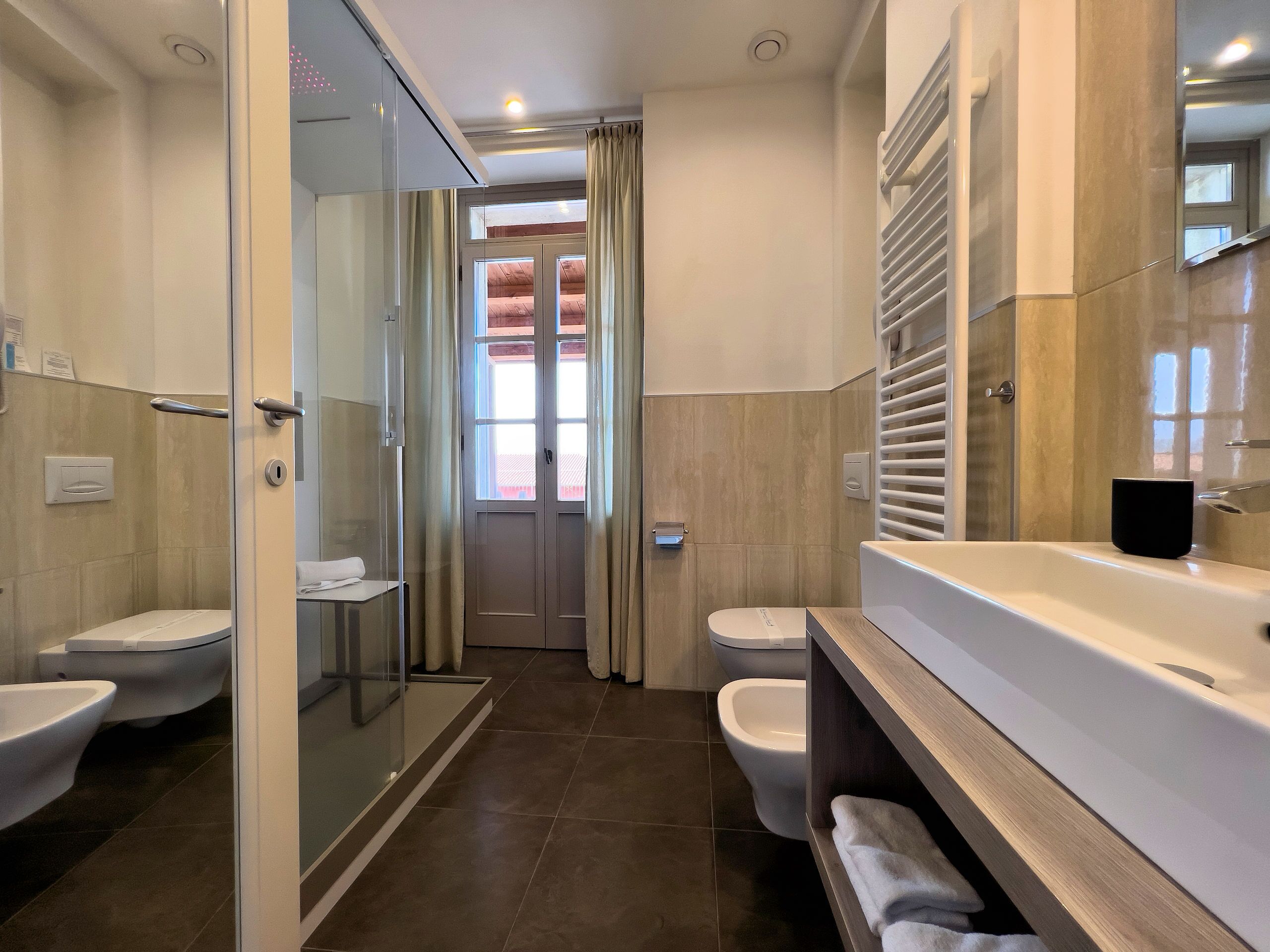 A modern bathroom with a glass-enclosed shower, two toilets, a bathtub, and a vanity with a mirror.