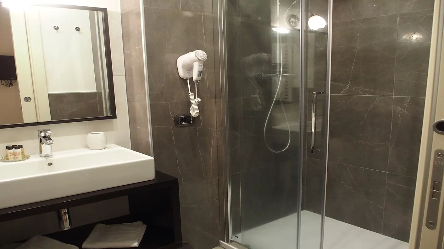 A modern bathroom with a glass-enclosed shower, a white sink, and a hairdryer mounted on the wall.