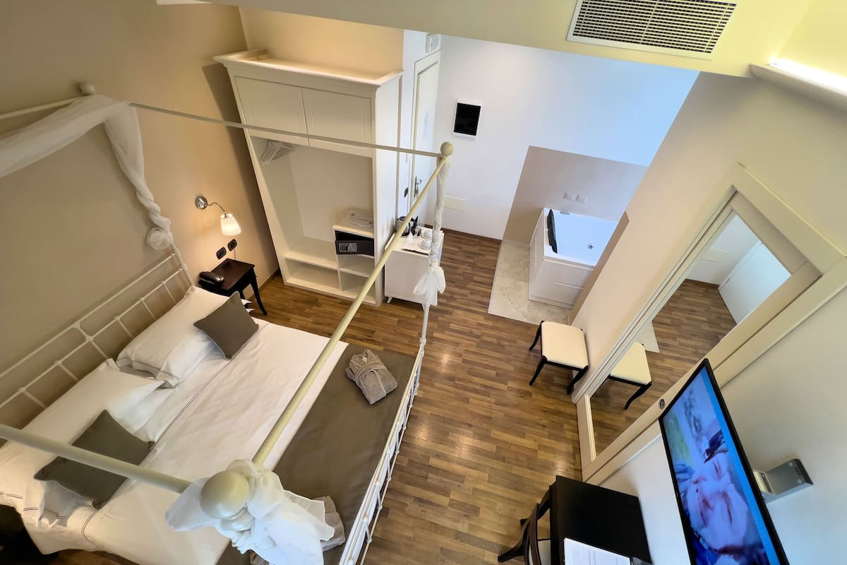 A hotel room with a bed, a desk, a chair, a TV, a bathroom, and a balcony.