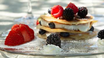 Una pila di pancake con frutti di bosco e panna montata su un piatto di vetro.