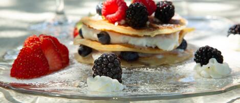 A stack of pancakes with berries and whipped cream on a glass plate.
