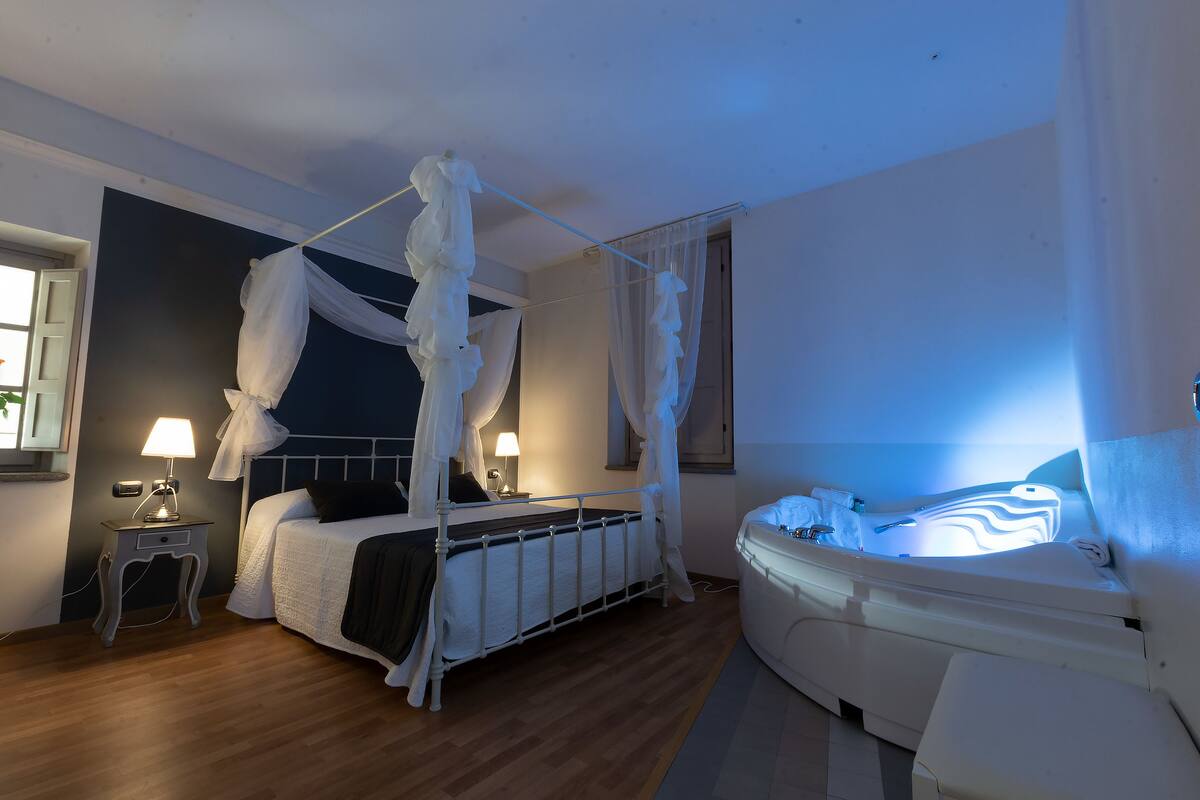 A bedroom with a four-poster bed, a bedside table with a lamp, and a massage chair.