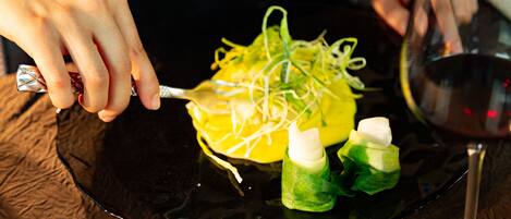 A person using a fork to eat a dish with green and yellow elements, possibly vegetables, on a black plate.
