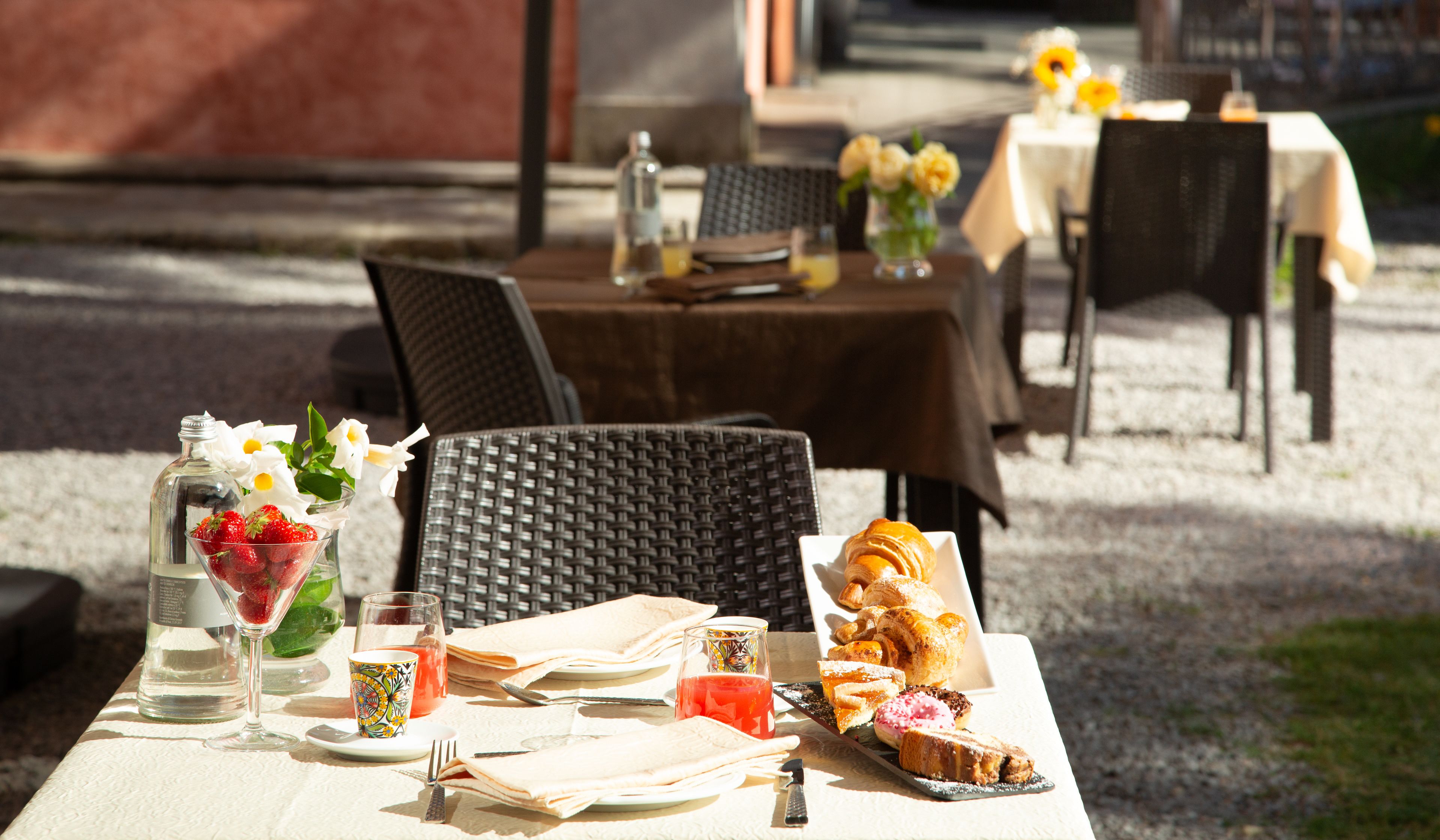 An outdoor dining area with wicker chairs, a table set with plates, cutlery, and a variety of pastries.