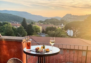 Un balcón con una mesa dispuesta para una comida, con vistas panorámicas a un pueblo y montañas.