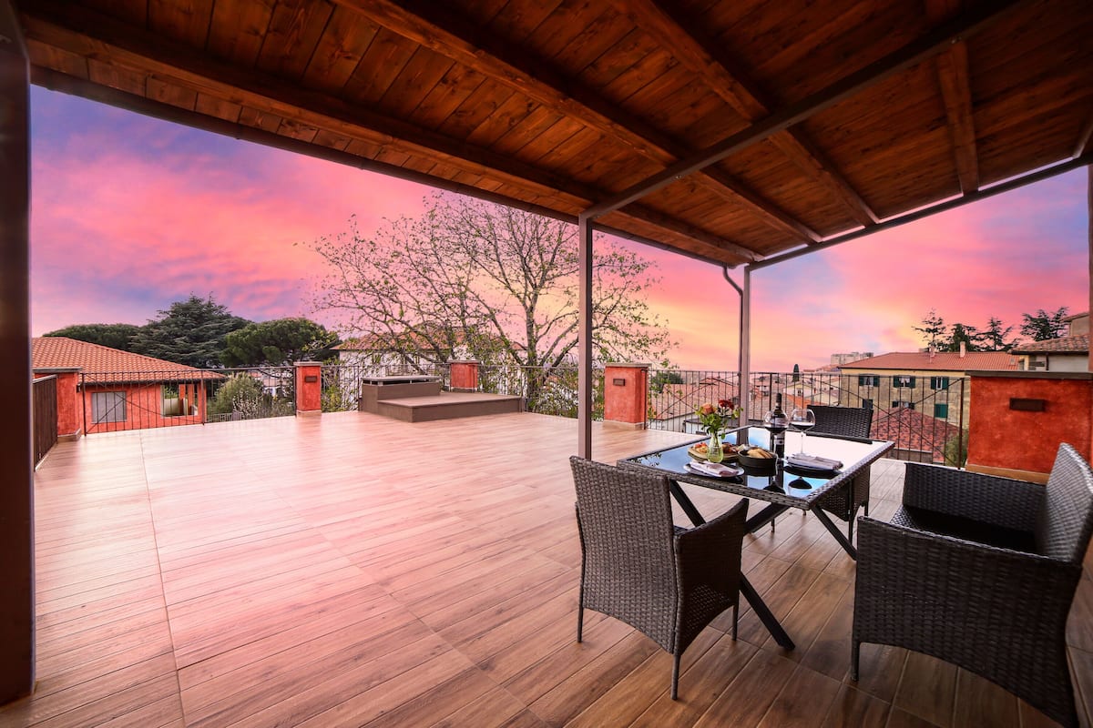 An open-air patio with a wooden deck, wicker furniture, and a table set for dining.