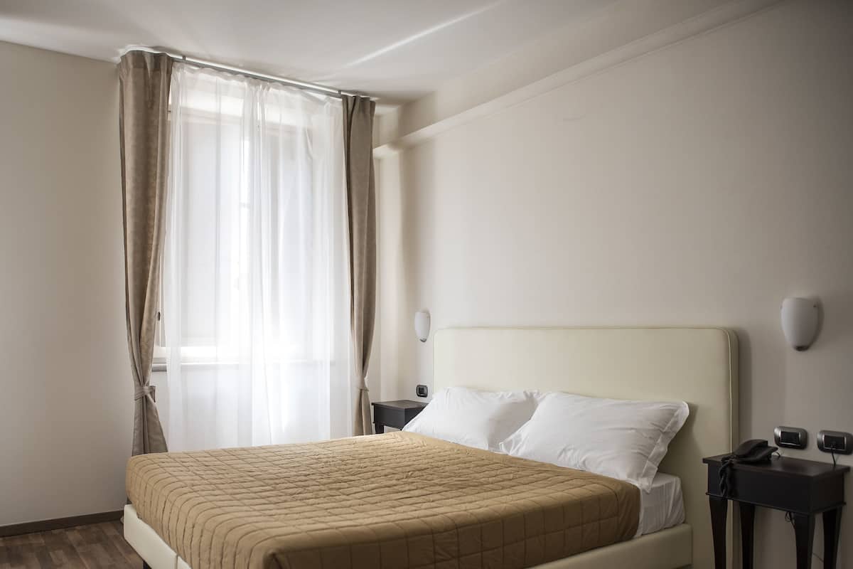A hotel room with a bed, a nightstand, a telephone, and a window with curtains.