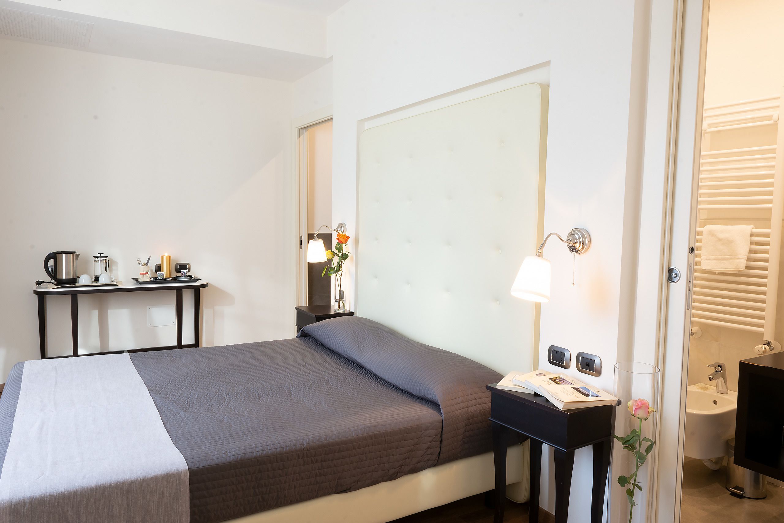 Una habitación de hotel con cama, mesita de noche, lámpara y baño a la vista a través de una puerta abierta.