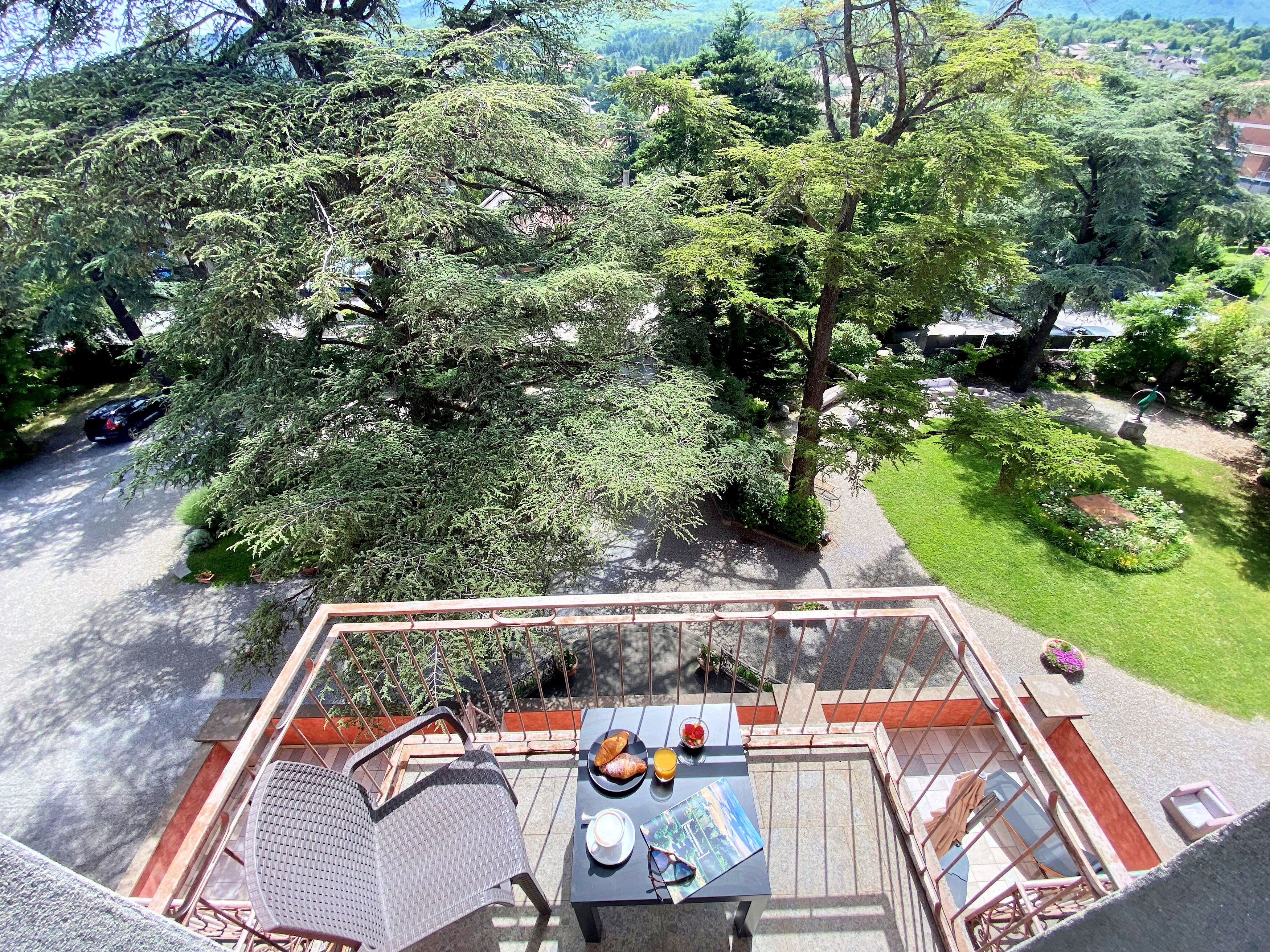 A terrace with a table, chairs, and a view of a lush garden and trees.