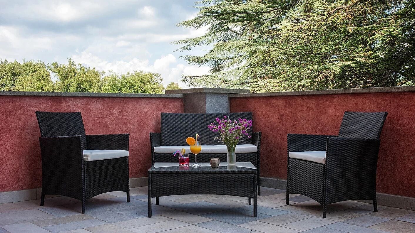 An outdoor seating area with wicker chairs and a table, a vase with flowers, and a drink.