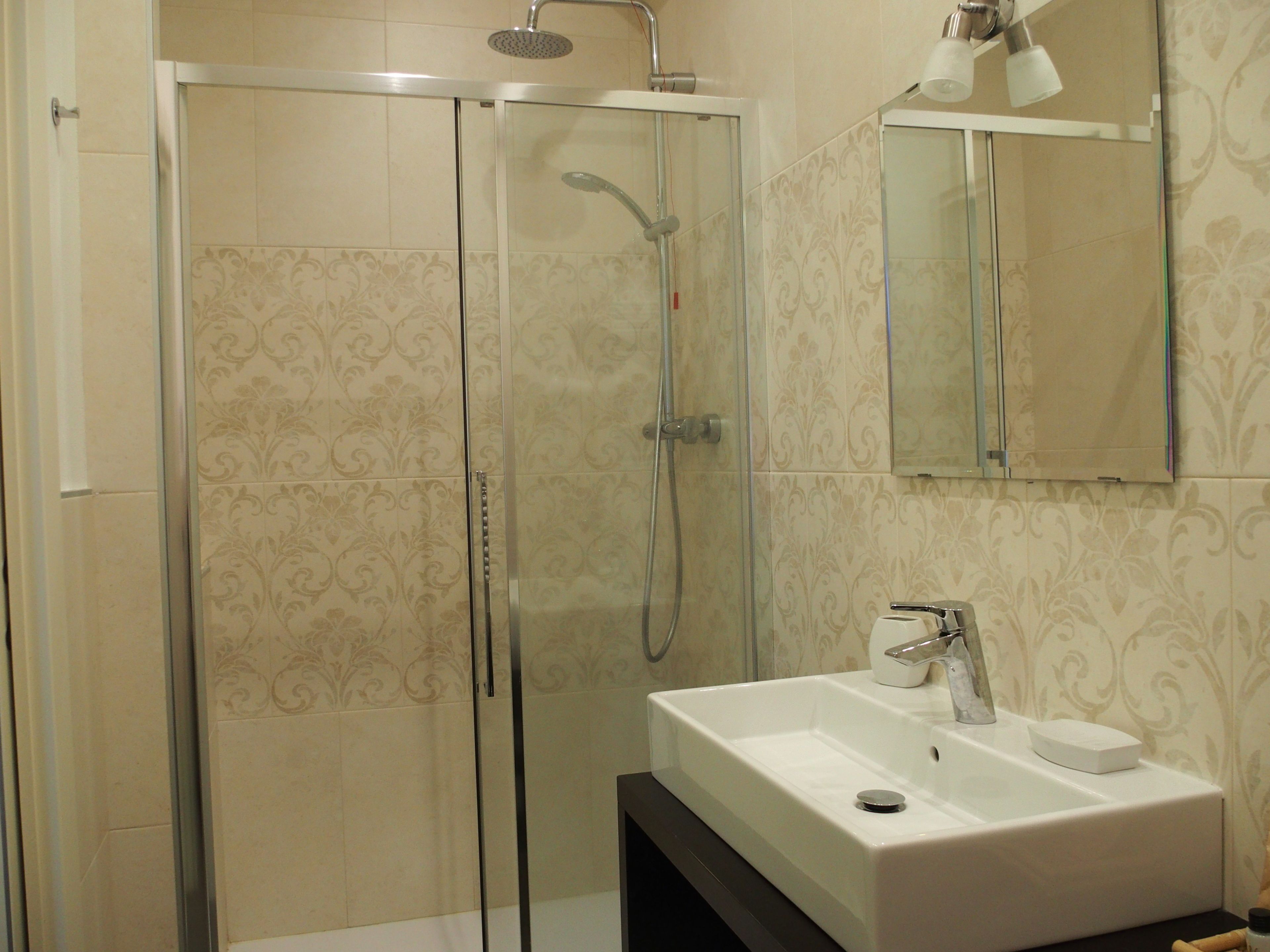 Un baño moderno con ducha envuelta en vidrio, un lavabo blanco y un espejo sobre él.