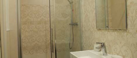 Un baño moderno con ducha envuelta en vidrio, un lavabo blanco y un espejo sobre él.